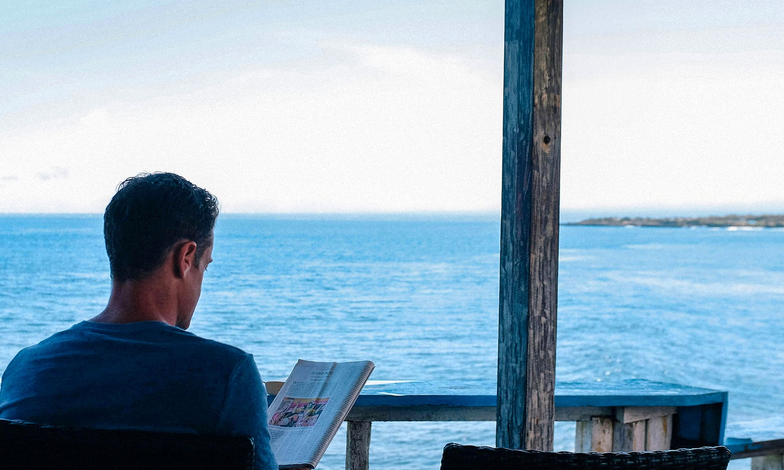 A man reading on a wooden porch above calm open water