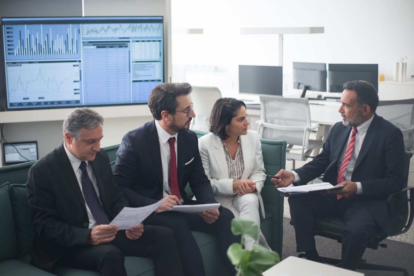 Four advisors in suits reviewing documents together in a modern office